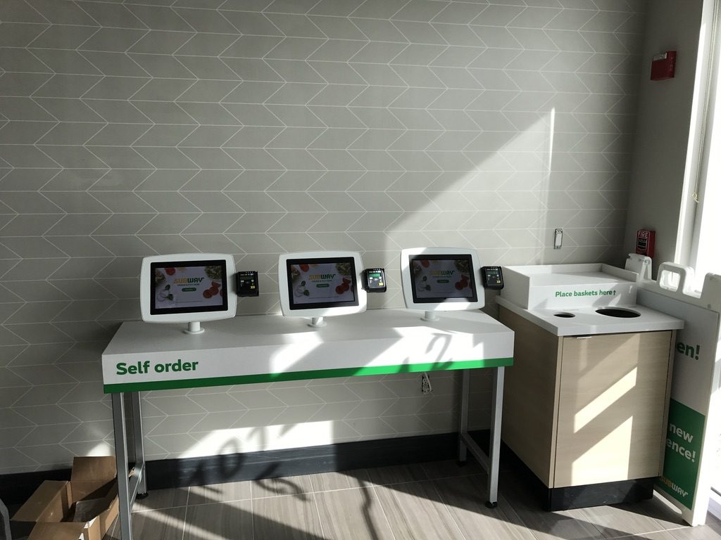 Three-kiosk self-order station with green Subway branding deployed in a restaurant